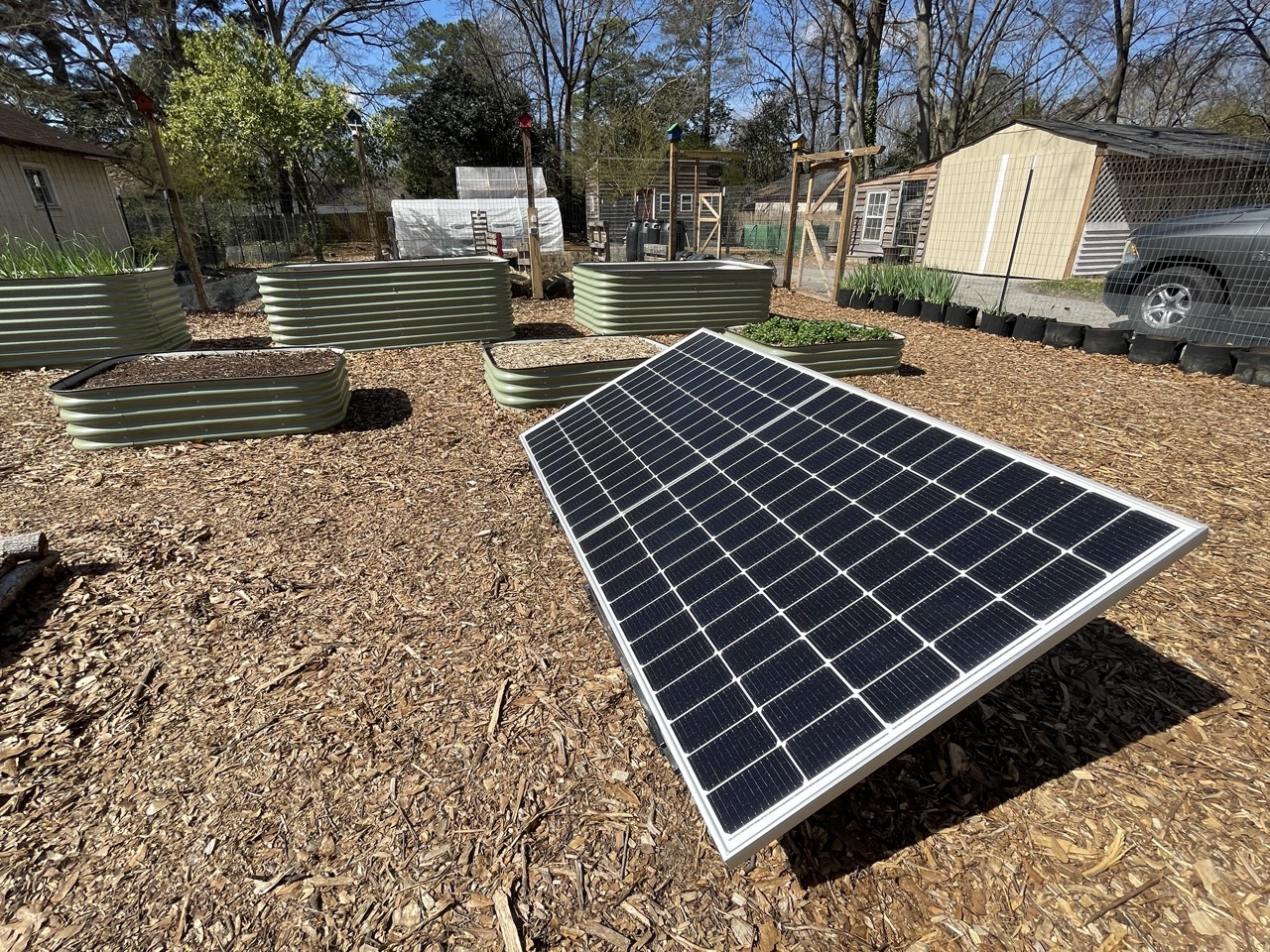Small photovoltaic solar panels mounted outdoors next to a garden area